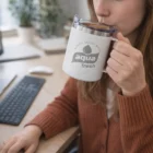 Woman in brown sweater sips from an Ace Vacuum Cups mug at her desk with a keyboard.