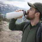 Man in outdoor gear uses a Reagan Vacuum Bottle while hiking on a mountain trail.
