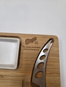 Wooden cheese board with Bega's best logo format, metal cheese knife, and ceramic dish.