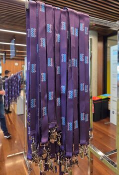 Purple lanyards with Minimum Order Quantity info hang on a metal rack at an indoor event.