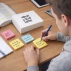 Person writes Biology exam Fri 10 on 204Mmx148Mm Bespoke Sticky Notes at a desk with books.