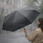 Person holding an Apex Ultimate Compact Umbrella in the rain, wearing a tan coat.