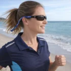 Woman jogging on a beach, wearing sunglasses with a Summer Promotional Item Glasses Strap.