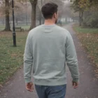 Man wears Wos Premium Crewss light gray sweatshirt while walking on a park path.