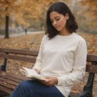 Woman wears Classic L/S Tees, reading on a park bench among autumn leaves.