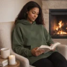 Woman wearing Relax Hoodies reads by the fire, enjoying coffee and a candlelit cozy vibe.