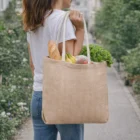 A woman carries a Skye Herringbone Pattern Jute Tote Bag filled with bread, lettuce, and bananas.