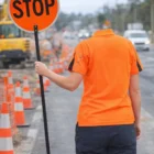 Worker in Women's Stylish Hi-Vis Polos holds STOP sign at road construction site with cones.