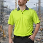 Man in a Unisex Koala Hi-Vis Polo and hard hat stands at a construction site.