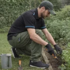 Man wears Utility Pants and gloves, gardening by flower bed with tools and watering can.