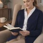 Woman in a Softstitch Button Cardigan sits in an armchair, reading and smiling softly.