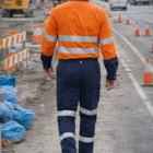 Construction worker in hi-vis gear and Ironcool Xt Pants– Stout Fit walks along traffic cone-lined road.