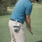 Man golfing with a Shield Caddies tee holder clipped to his pants, logo space visible.