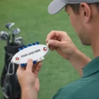 Man holding Oval Tees Caddies kit near golf clubs, perfect for caddies.