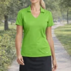 Woman in a bright green Nike Ladies Dri-Fit Vertical Mesh Polo and black skirt on a park path.