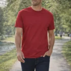 Man in Gildan Softstyle Adult Cotton T-Shirt and jeans walks on a tree-lined park path.