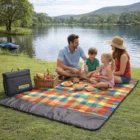 A family picnics by a lake on an Erinne Picnic Rug In Carry Bag with mountains behind.