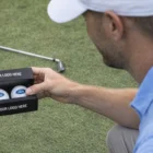 Man holding a Biz Card Pack with custom golf balls, golf club lying on grass nearby.