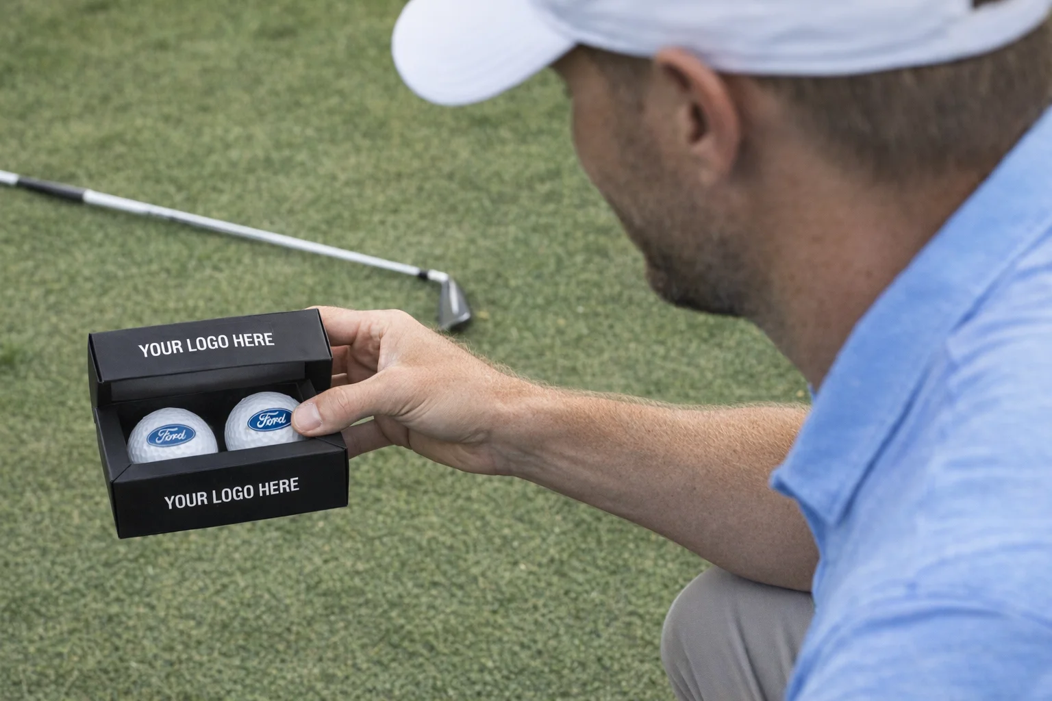 Man holding a Biz Card Pack with custom golf balls, golf club lying on grass nearby.