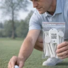 Man placing golf ball on tee, holding Tee Packs Unbranded labeled "Your Logo Here.