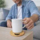 Man sets a white mug on a Round Bamboo Coaster atop a light-colored table.
