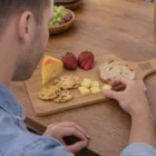A person sits at a table with Gourmet Eco Cheese Boards, crackers, bread, and strawberries.