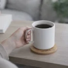 A person holds a white mug on Bamboo Coaster Sets at a light-colored table.