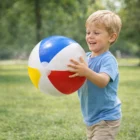 Smiling boy in blue shirt holds a Bondii Beach Balls 48cm outdoors on grass.