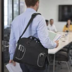 Man with a black Expedit Conference Satchel enters a meeting room holding papers.