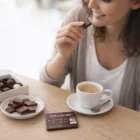 Woman smiling, holding Business Card Sized Chocolates by her coffee, with more on the table.