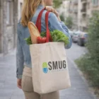 Woman carries Calico Show Bag of groceries with SMUG Supplements logo on a city sidewalk.