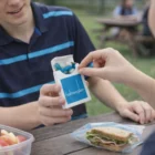 Two people share blue pills from 25G Recyclable Jelly Bean Boxes at a picnic table.
