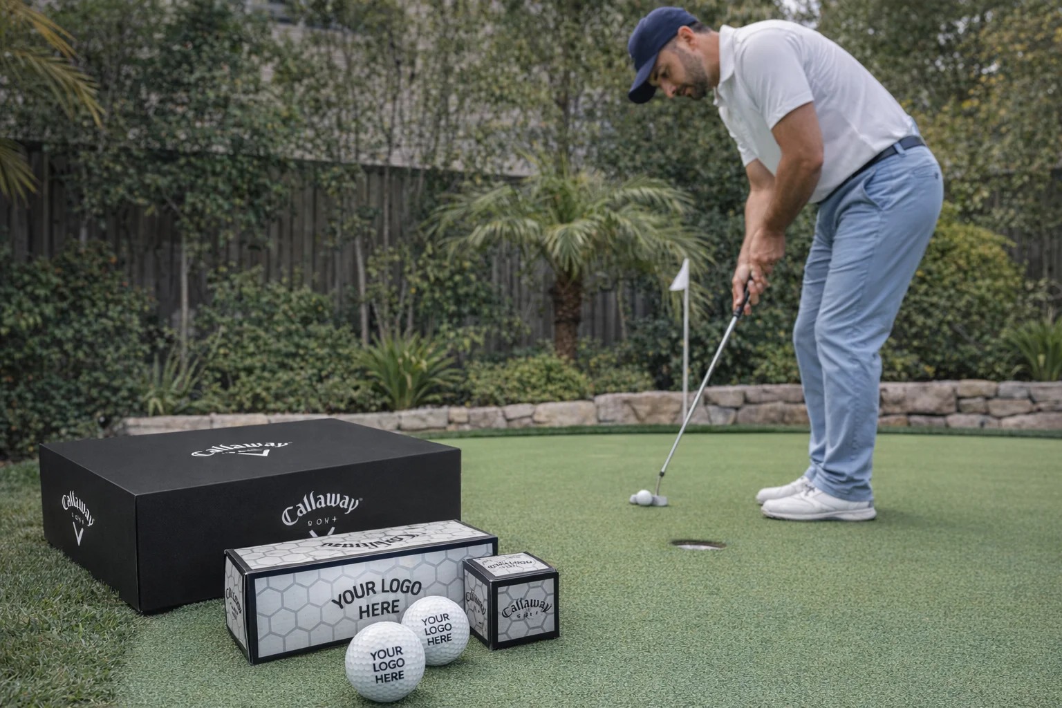 Man placing golf ball on green with Golf Balls Callaway and boxes displayed in the foreground.