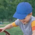 Smiling boy in a blue cap plays outside, wearing our Childrens Soft Caps.