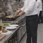 Chef in Lee Men's Functional Chef Pants cooks at stove with pots and fresh ingredients.