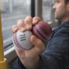 Man holding two Stress Balls Cricket Red with YOUR LOGO HERE text, one red and one white.