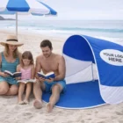 Family reading books on Bondi Beach under Bondi Beach Shades with custom Your Logo Here sign.