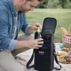 Man places a wine bottle in the Oslo Bottle Cooler Bag + Opener during a picnic on the grass.