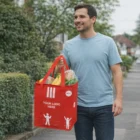 Man walking outside holding a red Eco Friendly Promo Chiller Bag filled with groceries.