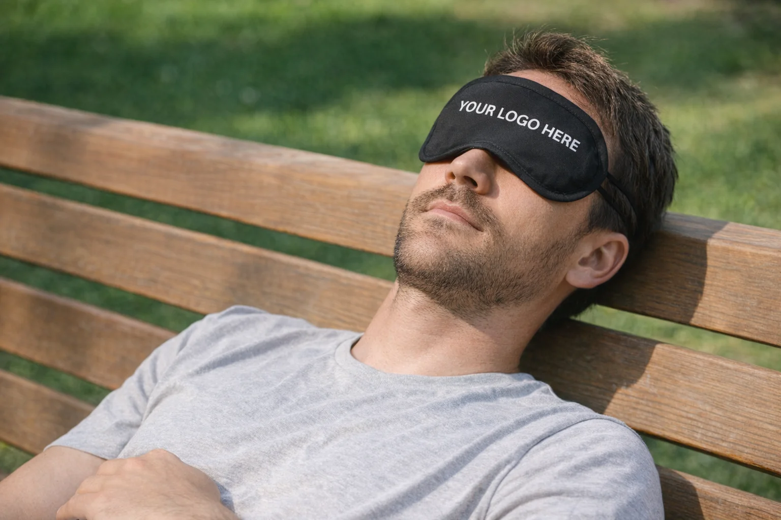 Man in gray shirt on bench wearing an Eye Mask that says YOUR LOGO HERE.