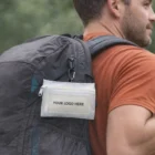 Man in orange shirt with Clip On Care Kit Brandable Products attached to backpack.