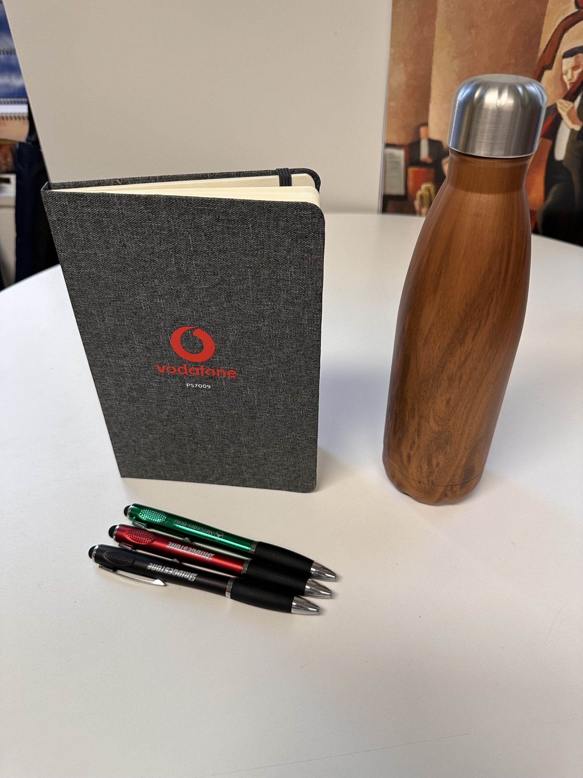 A wooden bottle, a Vodafone notebook, and pens suggest a branded merchandise forecast.