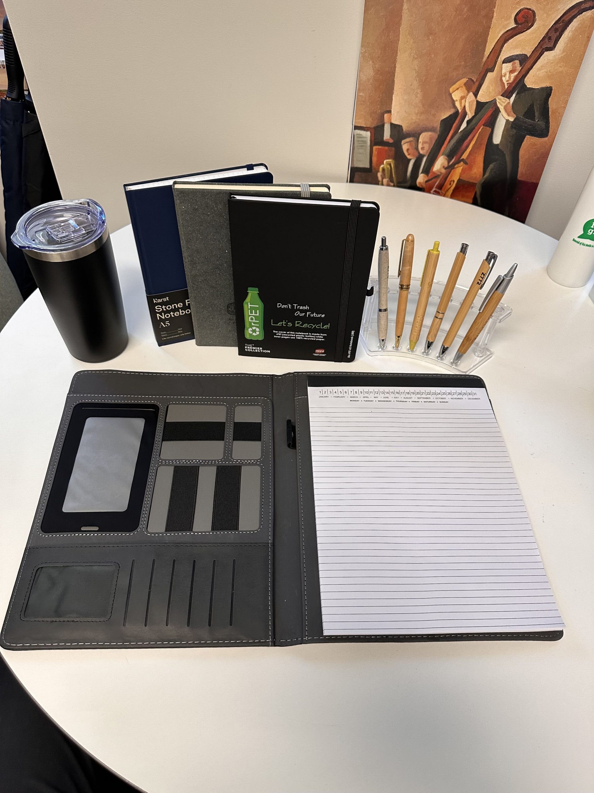 Open notepad, pens, notebooks, and forecast branded merchandise on a round white office table.