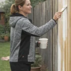 Woman painting a fence outdoors in stylish Wee Iii Aiwx Workwear Jackets, holding white paint.