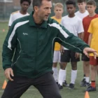 Coach in Tyu Ii Adults Warm Up Jackets trains youth players on a field with cones.