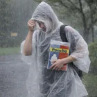 Person in Reusable Polythene Ponchos holds a poncho package while walking in heavy rain.