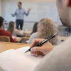 Student taking notes with a Lotus Deluxe Pen as teacher speaks in the background.