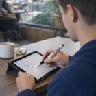Writing study notes on a tablet with a Zonko Stylus Pen in a café, coffee cup nearby.