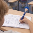 Child doodling in a notebook with a blue Kids Promotional Pen Mop Toppers.