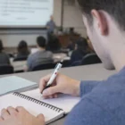 Student taking notes in a lecture hall with a Jubilee Full Colour Printed Pen and notebook.